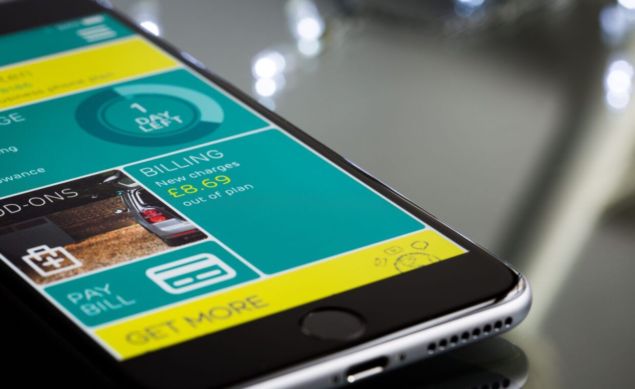 Close-up of a smartphone displaying a billing app interface on a reflective surface.