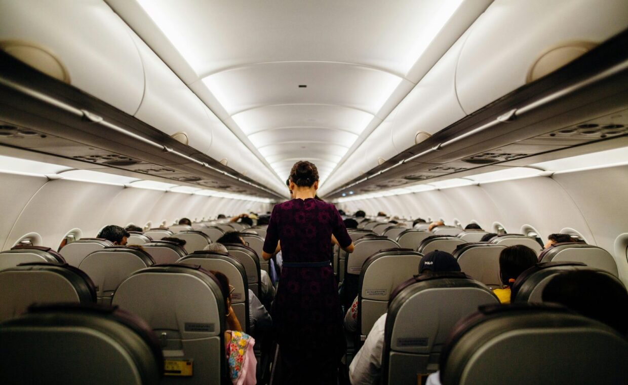 Interior view of an airplane cabin with passengers seated and a flight attendant walking down the aisle.