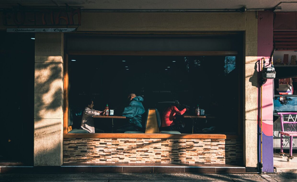 People dining inside a cozy cafeteria in Ciudad de México, viewed through a large window.