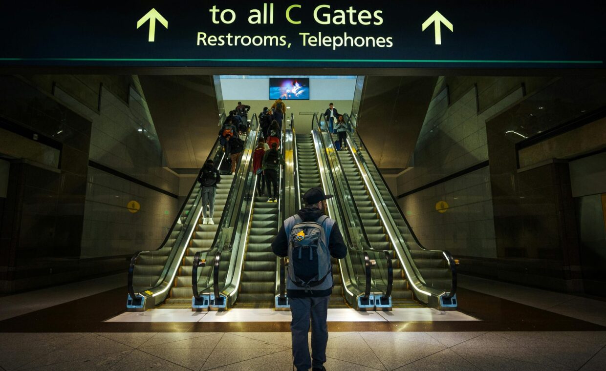 Man with backpack at airport escalator heading to C Gates, showcasing modern architecture.