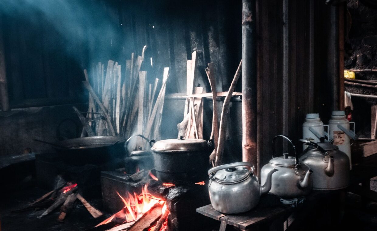 Traditional rustic kitchen with woodfire cooking and metal teapots, creating a warm, nostalgic ambiance.