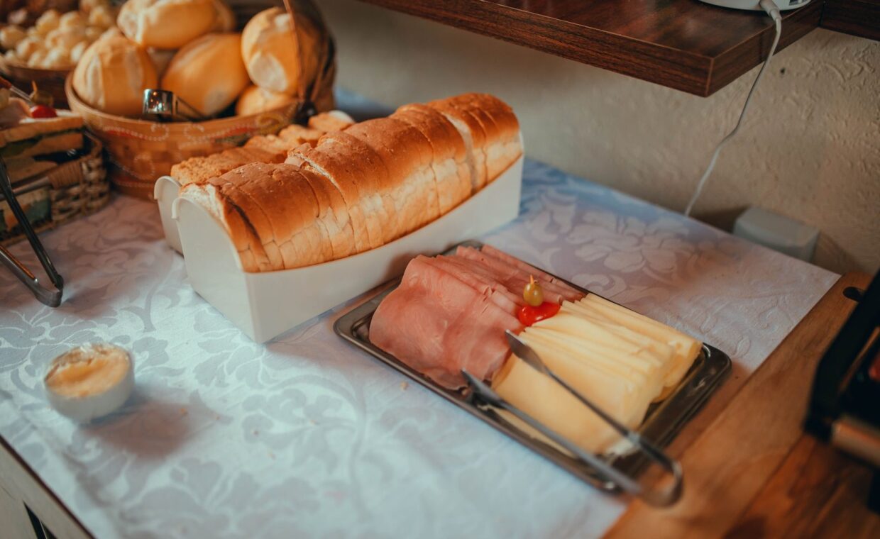 A delightful continental breakfast setup featuring sliced bread, ham, cheese, and rolls on a linen-covered table.