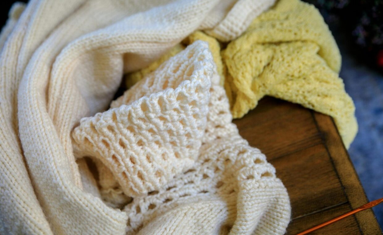 A close-up of soft wool knit sweaters in neutral tones on a rustic wooden table.