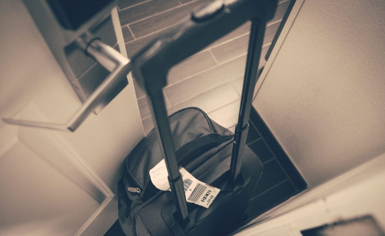 Travel suitcase with tag by hotel door, symbolizing travel or business trip.
