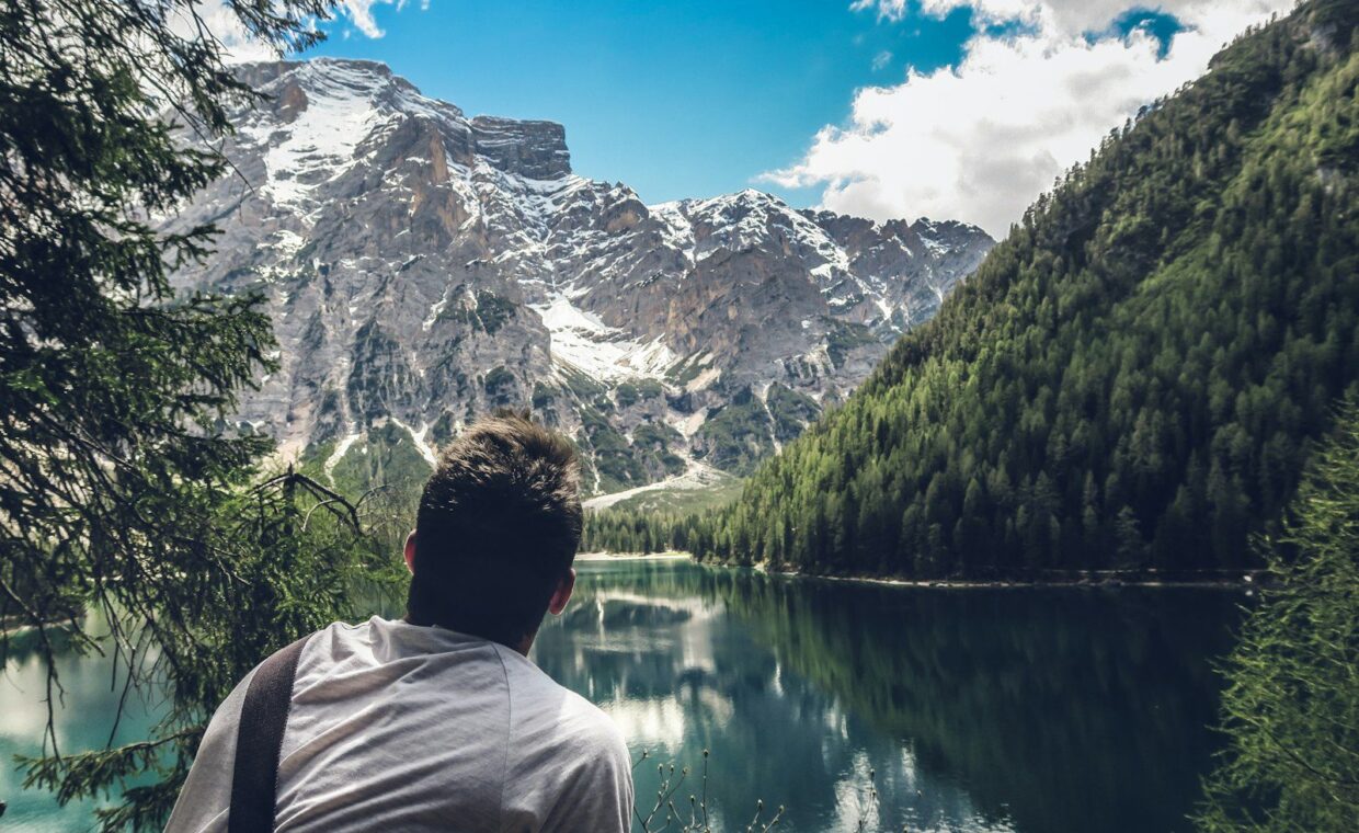 man in white shirt sitting on rock looking at lake and mountains during daytime