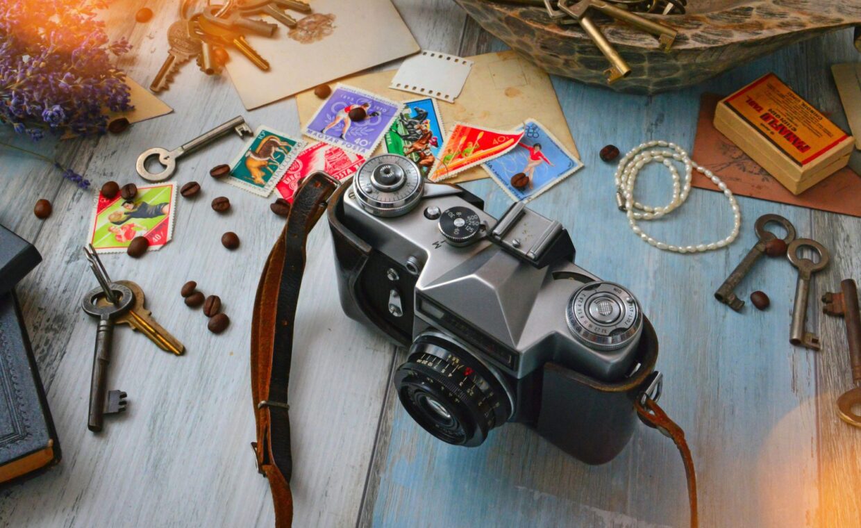 A vintage camera surrounded by an assortment of keys, stamps, and coffee beans on a wooden table.
