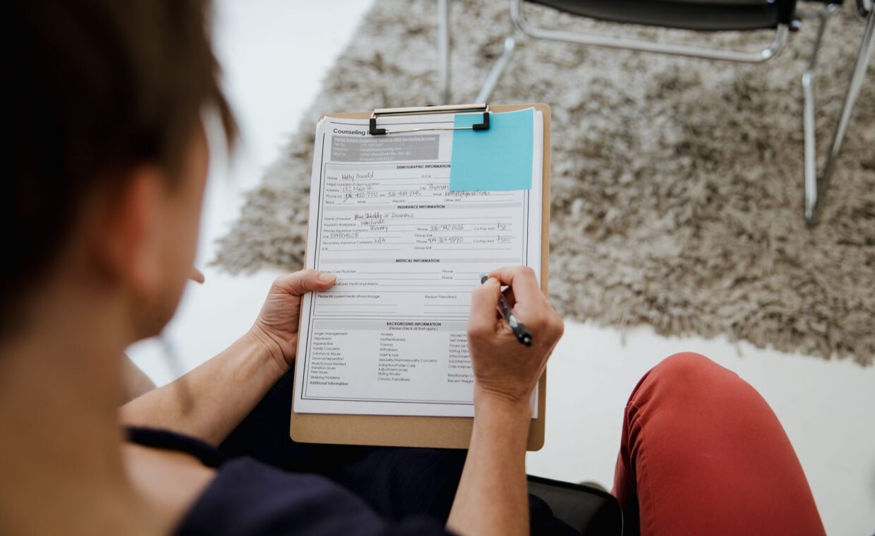 An adult woman writing on a counseling form during a business appointment in an office setting.