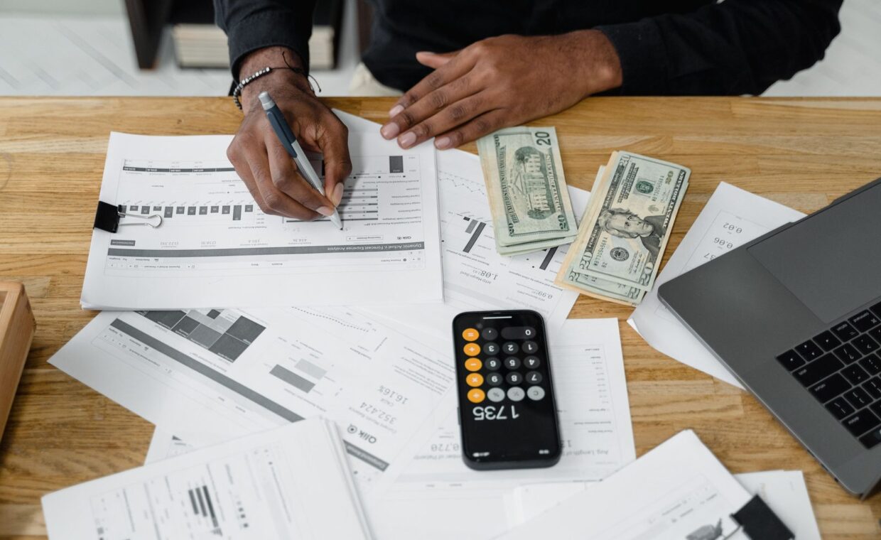 Man working on financial reports with calculator, money, and laptop on a desk.